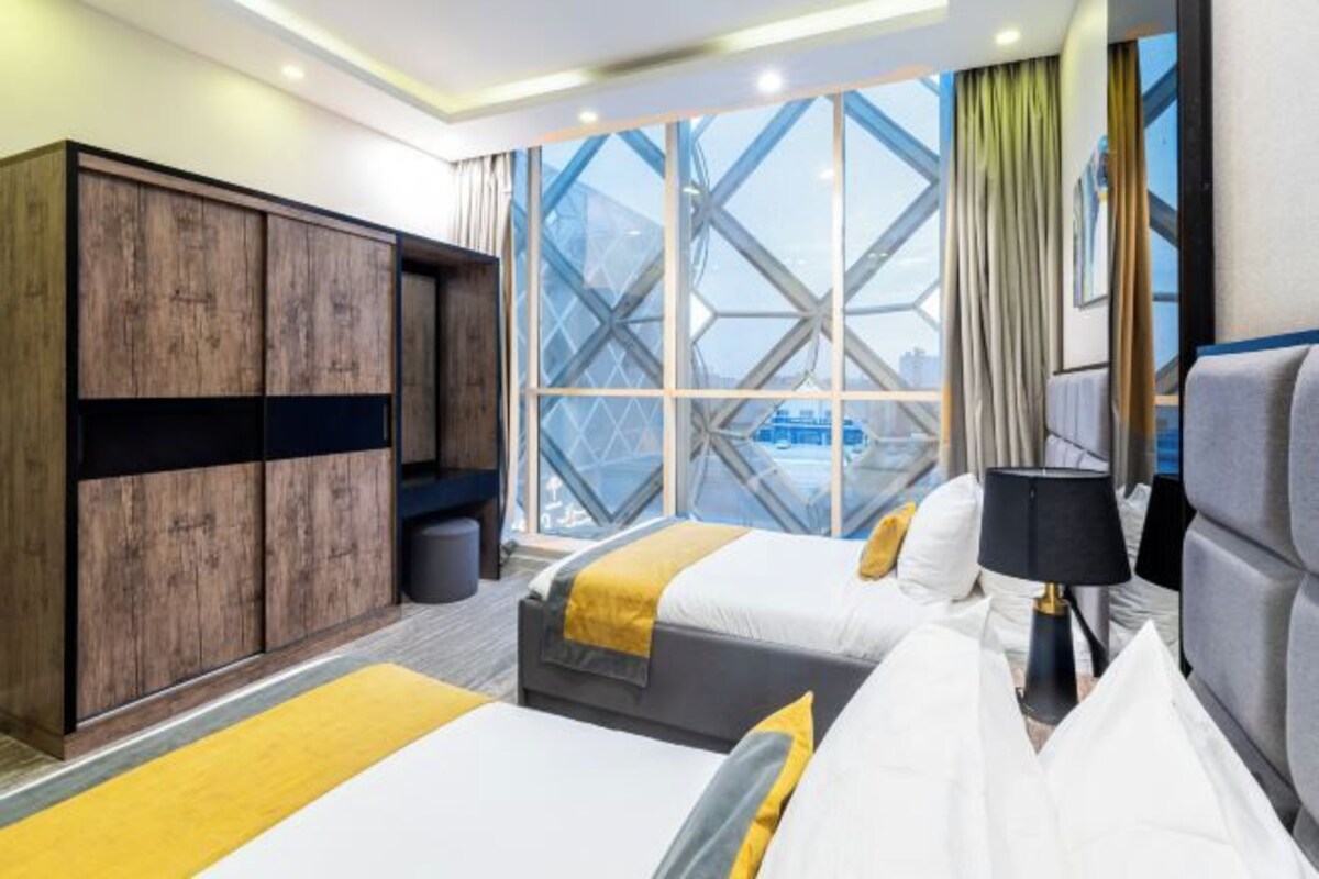 A hotel room with two beds, a wardrobe, a window with a view, and a lamp.