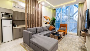 Una sala de estar moderna con un sofá modular, una mesa de centro, un sillón naranja, un televisor y un ventanal con vista a una noria.