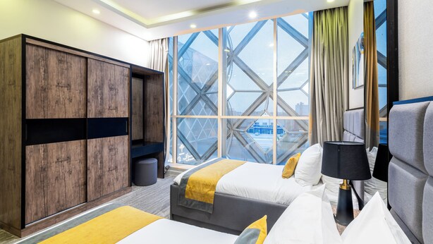Una habitación de hotel con dos camas, un armario, una ventana con vistas y una lámpara.