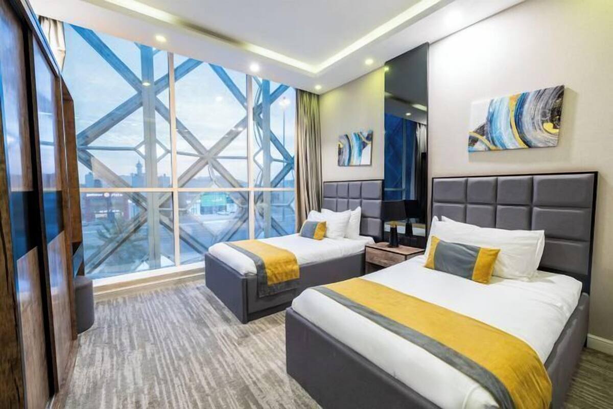 A hotel room with two beds, a large window with a city view, a modern headboard, and a painting on the wall.