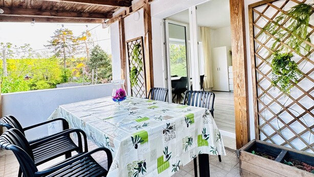 Eine Terrasse im Freien mit einem Tisch, der mit einer gemusterten Tischdecke bedeckt ist, umgeben von Stühlen.