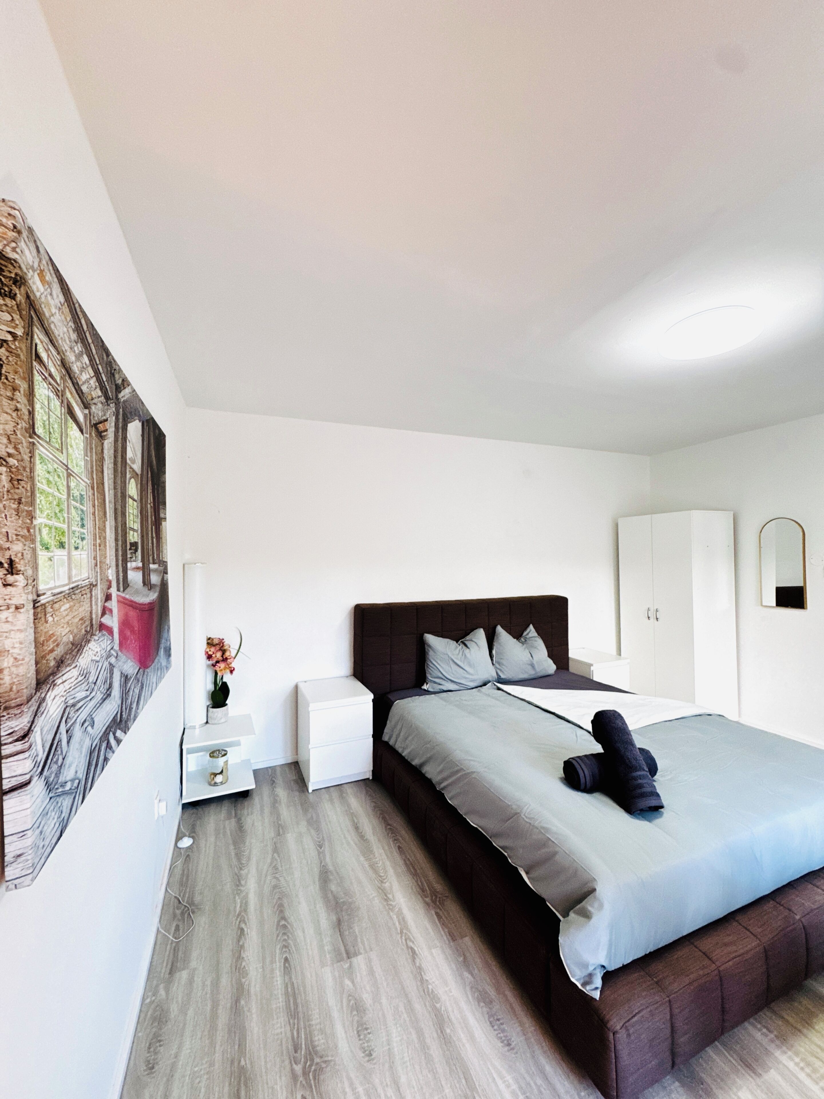 A modern bedroom with a large bed, a nightstand, a wardrobe, and a mural on the wall.