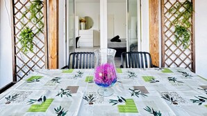 Ein Essbereich mit einem Tisch für zwei Personen, einer dekorativen Vase und Blick in einen Raum mit Bett und Schminktisch.