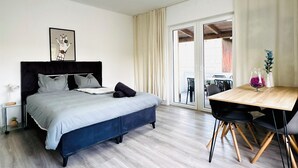 Ein Schlafzimmer mit Bett, Nachttisch, Lampe und Blick nach draußen.