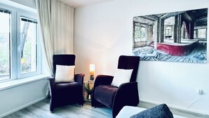 Ein Zimmer mit einem Bett, zwei Sesseln, einem Tisch mit Lampe und einem Bild an der Wand.