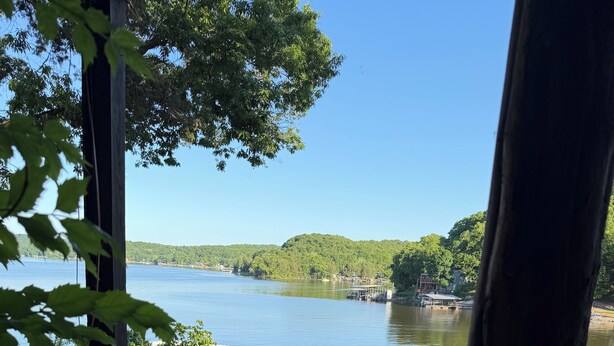 Vista de um lago com um cais, cercado por vegetação e céu claro.