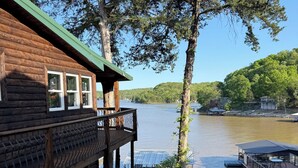 Uma cabana de madeira com varanda e vista para um lago, rodeada por árvores.