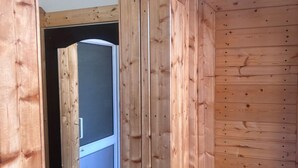 A wooden interior with a visible door leading to another room, a power outlet on the wall, and a trash bin. - Aaroham Retreat (Mussoorie)