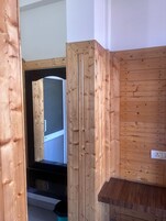 Un interior de madera con una puerta visible que da a otra habitación, un enchufe en la pared y un cubo de basura.