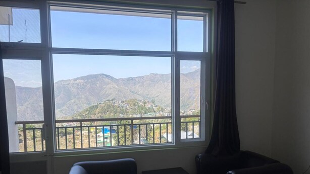 A hotel room with a large window, a bed, a desk, and a chair. - Aaroham Retreat (Mussoorie)