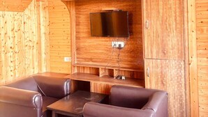 A room with a wooden wall, a flat-screen TV mounted above a wooden bench, and leather seating. - Aaroham Retreat (Mussoorie)