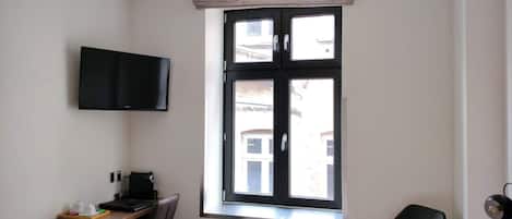 Une chambre d’hôtel équipée d’un lit, d’un bureau, d’une chaise, d’un téléviseur fixé au mur et d’une fenêtre donnant sur les bâtiments environnants.