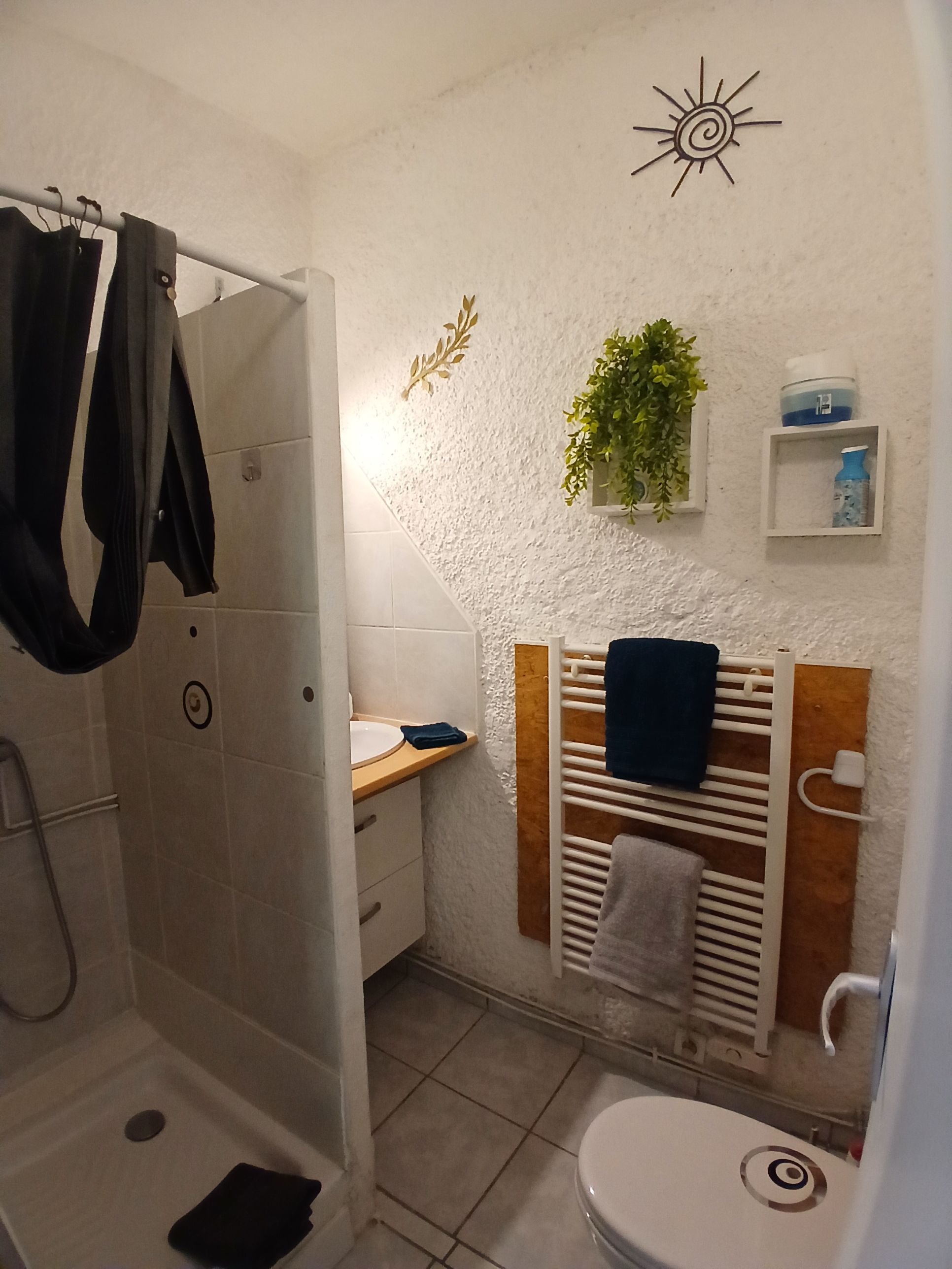 A bathroom with a shower, a sink, a toilet, a towel rack, and a small shelf with toiletries.