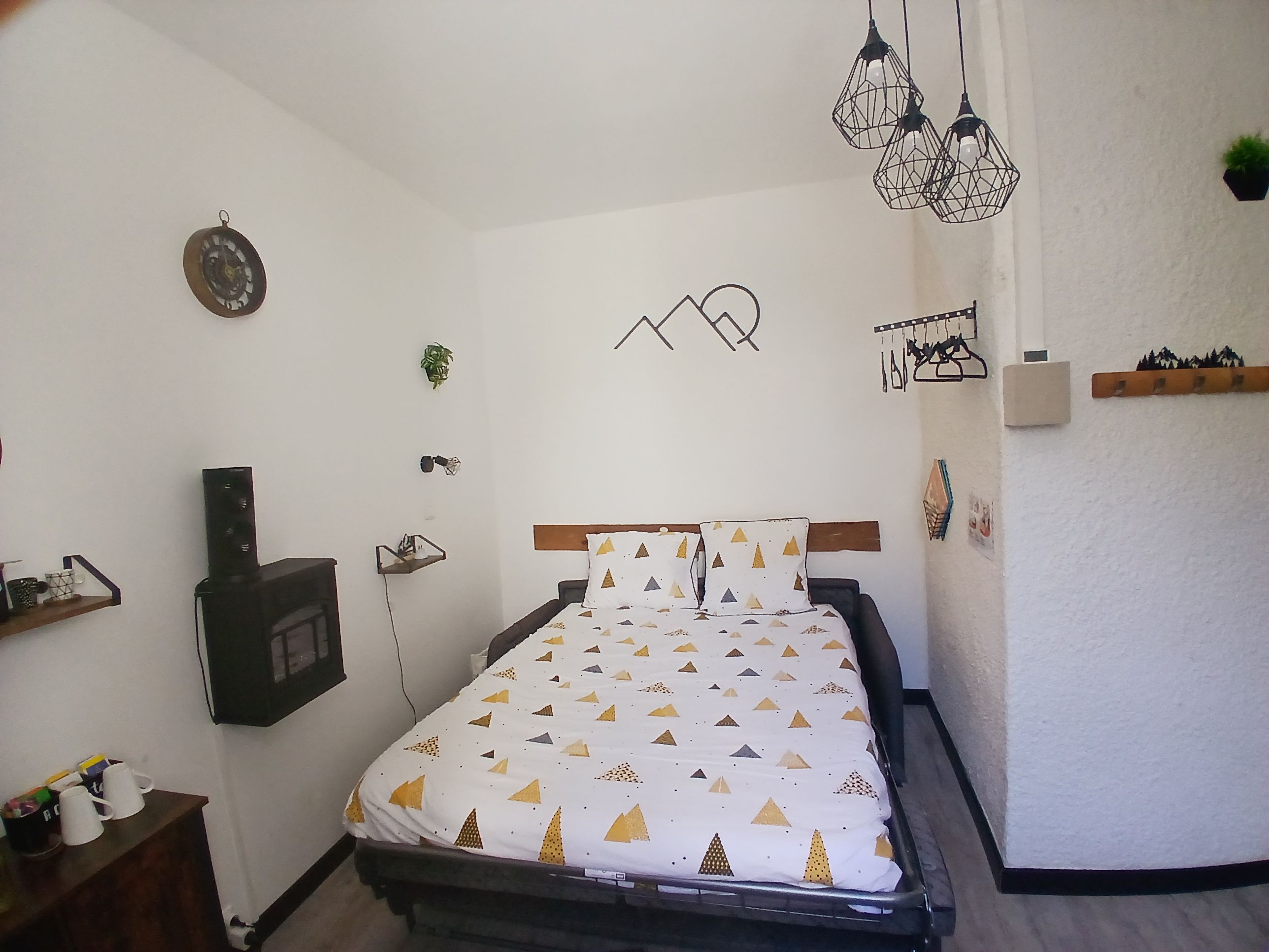 Une chambre à coucher comprenant un lit, un haut-parleur fixé au mur, un luminaire suspendu et un élément décoratif mural.