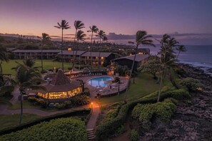 Un resort con piscina, palmeras y vista al océano al atardecer.