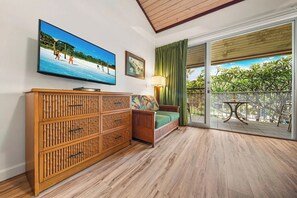 Una habitación con un armario de madera, un sofá, un televisor y un balcón con vistas a zonas verdes.