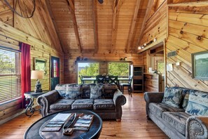 Ein Interieur einer Blockhütte mit einer Sofagarnitur, einem Esstisch und Blick ins Freie.