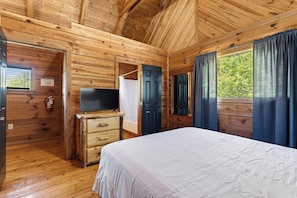 Ein Schlafzimmer in einer Holzhütte mit Bett, Kommode, Fernseher und einer Tür, die nach draußen führt.