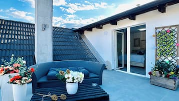 A rooftop patio with a sofa, potted plants, and a chimney.