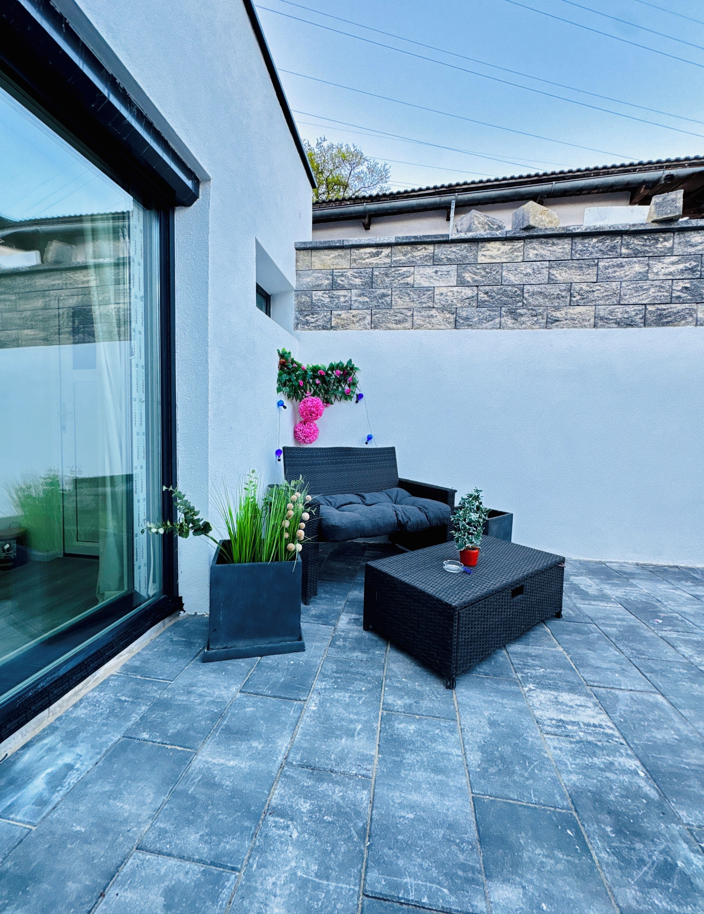 A modern outdoor seating area with a stone wall, a glass door, and potted plants.