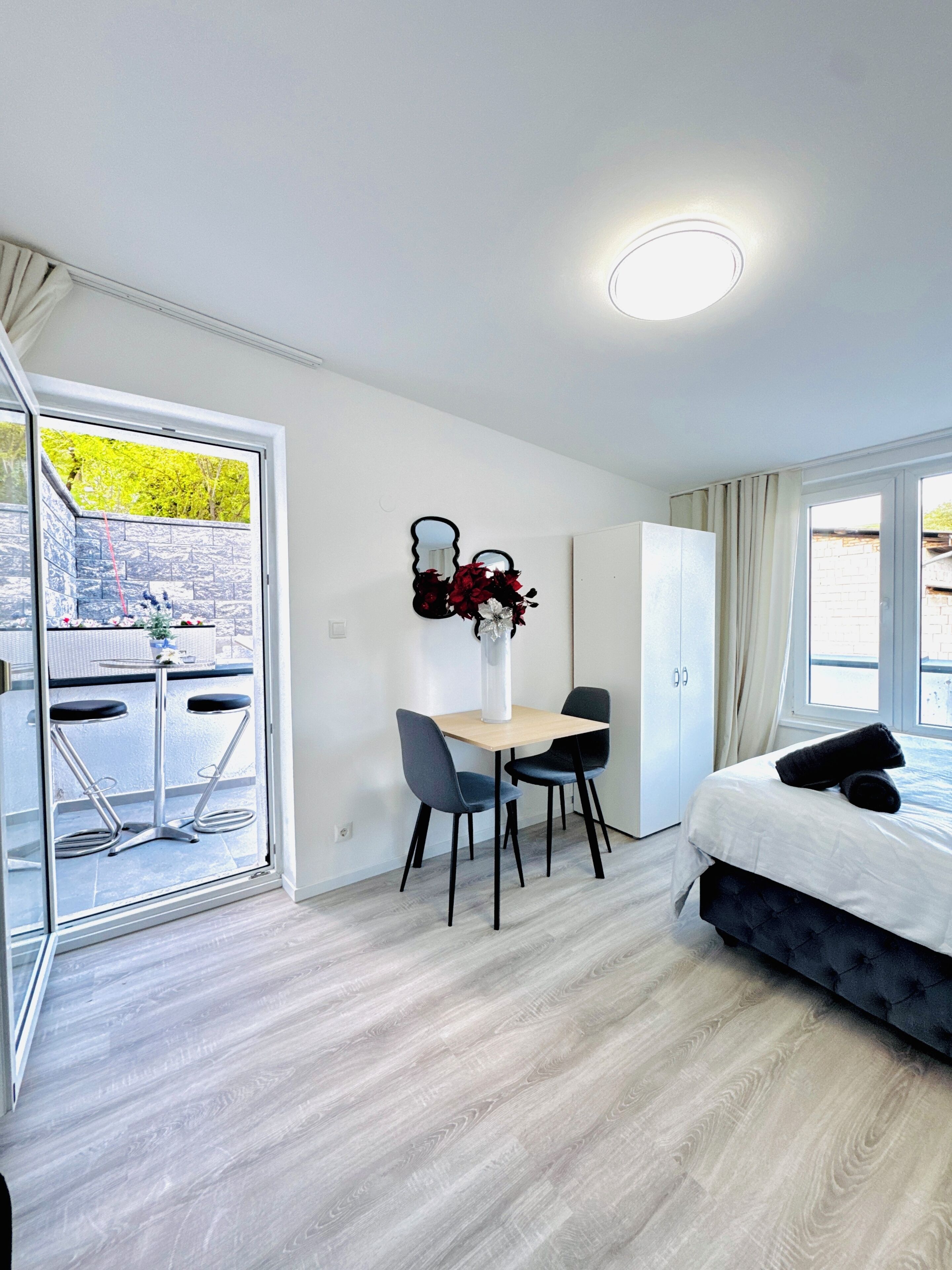 A modern hotel room with a balcony, a dining area, and a bed.