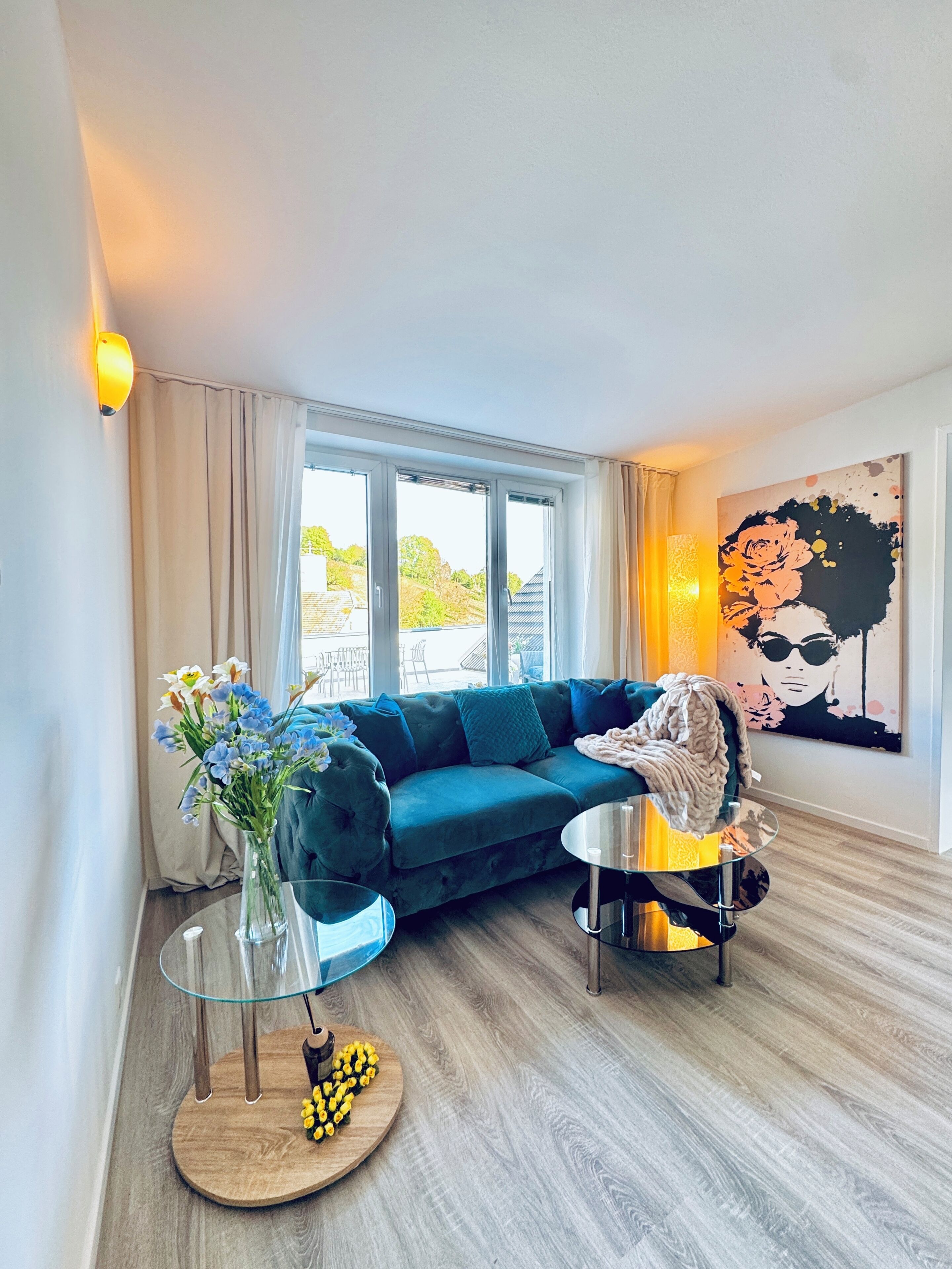 Een moderne woonkamer met een blauwe bank, een glazen salontafel en een schilderij aan de muur.