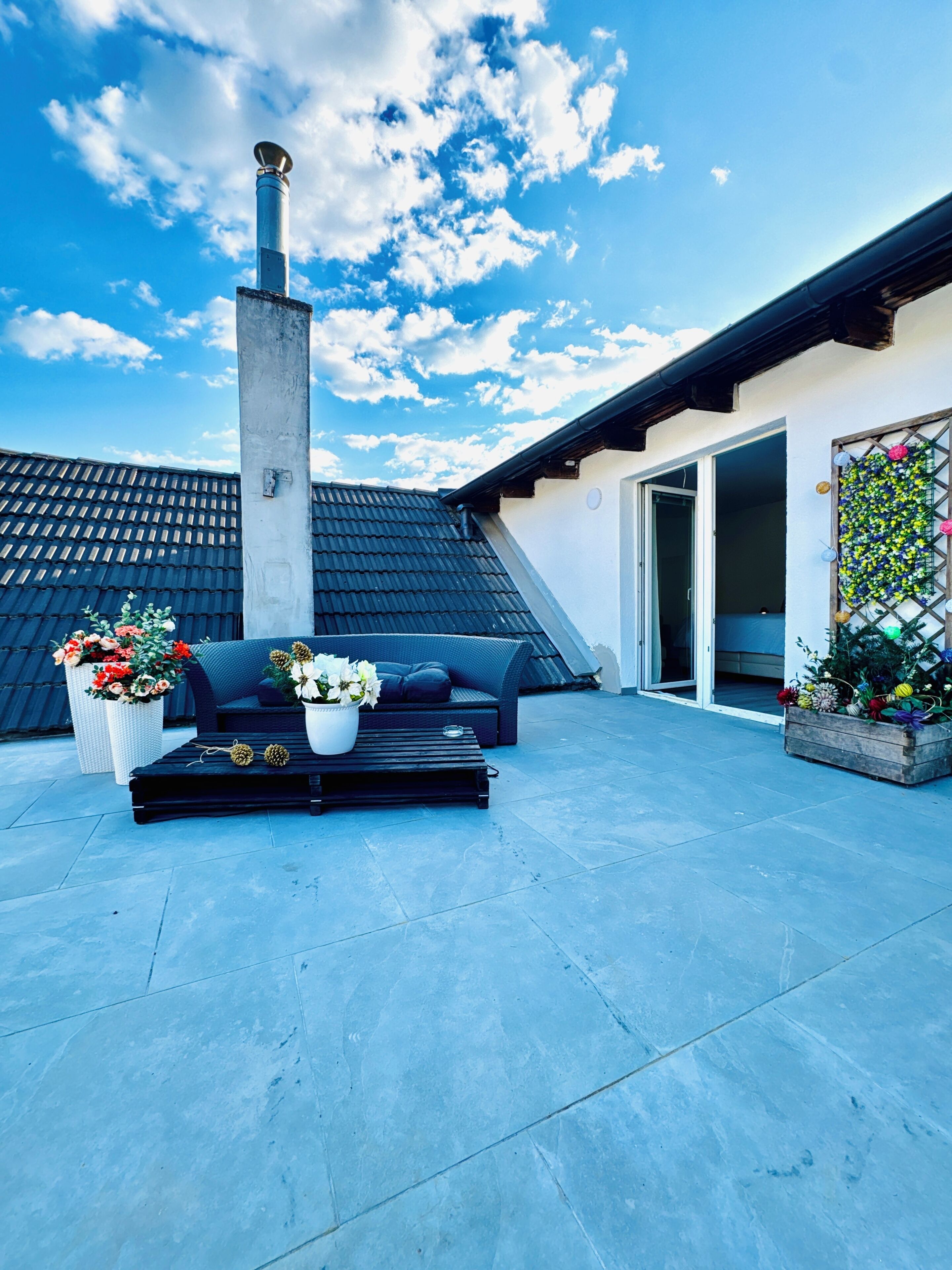 A rooftop patio with a black sofa, white flower pots, and a chimney.