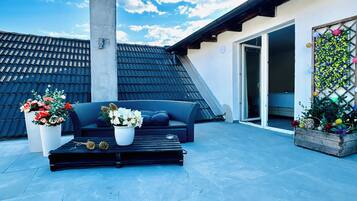 A rooftop patio with a black sofa, white flower pots, and a chimney.