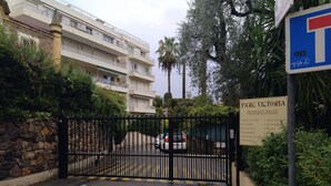 Une entrée fermée par un portail donnant accès à un quartier résidentiel, avec un panneau indiquant les noms des immeubles.