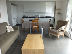 A modern living room with a sofa, a wooden coffee table, and a dining area with a table and chairs. - Beautiful apartment 100m from the beach, air conditioning, parking, 53m2, balcony and terrace. (Cannes)