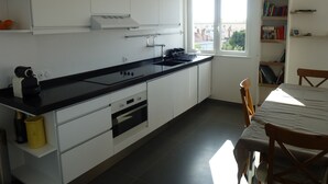 Une cuisine moderne avec des meubles blancs, un plan de travail noir et une fenêtre donnant sur la ville.