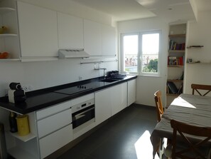 A modern kitchen with white cabinets, a black countertop, and a window with a city view. - Beautiful apartment 100m from the beach, air conditioning, parking, 53m2, balcony and terrace. (Cannes)