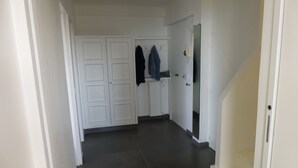 Un couloir avec une porte blanche, un porte-manteau et un téléphone blanc.