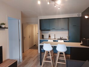 Une cuisine moderne avec des meubles bleus, un plan de travail blanc et deux tabourets de bar blancs.