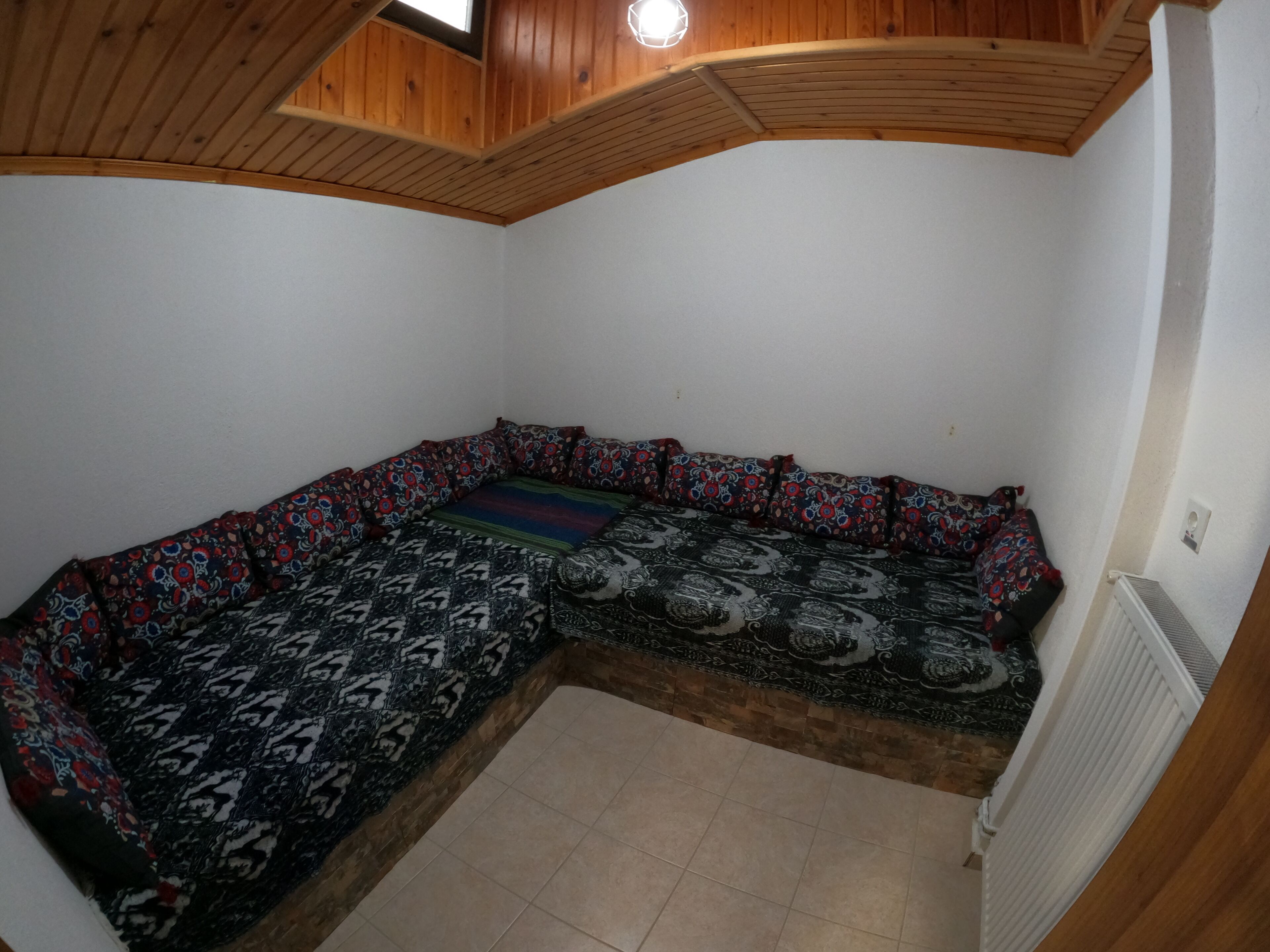 Habitació amb sofà d'angle, sostre de fusta, parets blanques i un radiador.