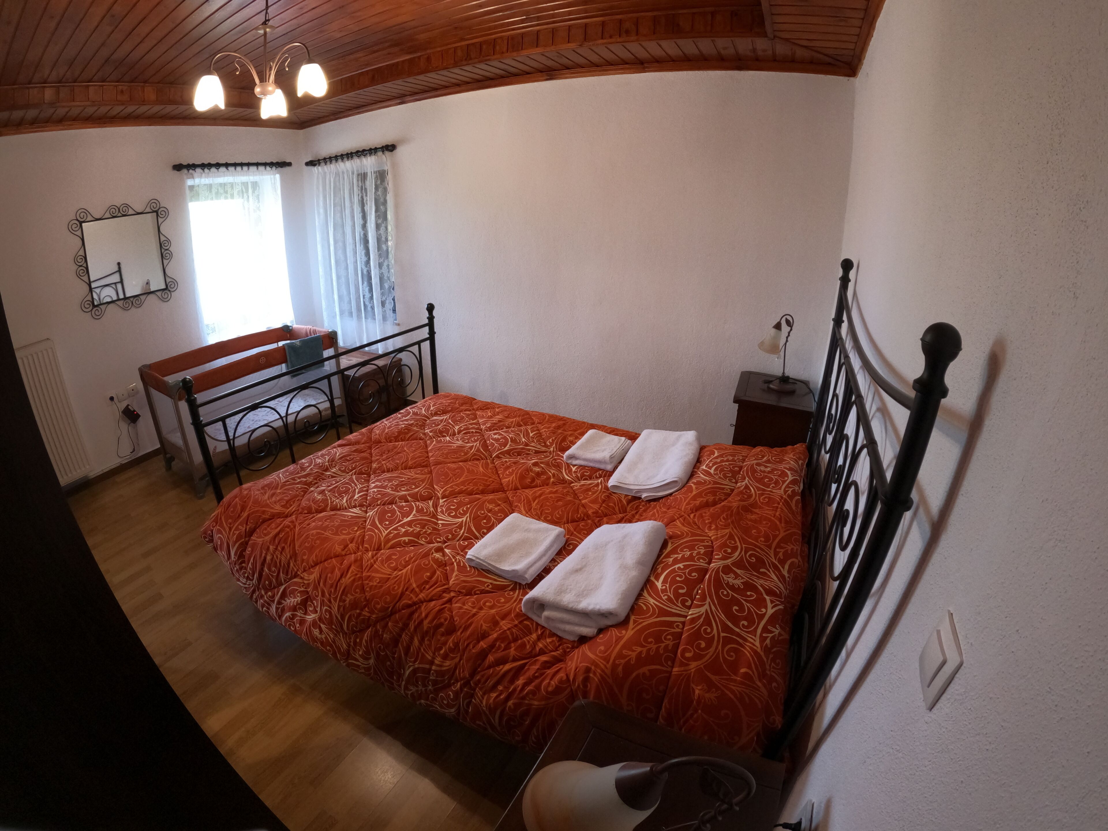 A bedroom with a bed, a bedside table, a lamp, a mirror, and a window with curtains.