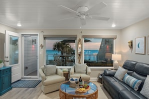 Ein Wohnzimmer mit Glastisch, zwei Sofas, einem Deckenventilator und Meerblick.