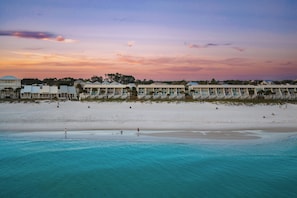 Ein Hotel direkt am Strand mit mehreren Gebäuden, einem Sandstrand und klarem, türkisblauem Wasser.
