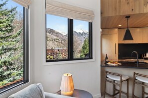 A modern kitchen with a large window, bar stools, and a lamp. - Shared Hot Tub + Mtn Views | Walk to Gondola + River Trail | (Telluride)