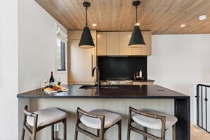 A modern kitchen with a central island, bar stools, pendant lighting, and a black backsplash. - Shared Hot Tub + Mtn Views | Walk to Gondola + River Trail | (Telluride)