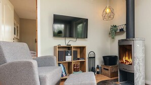 A living room with grey upholstered furniture, a flat-screen TV, a modern fireplace, and a wooden bookshelf. - 8 Person Holiday Home in Stege (Stege)