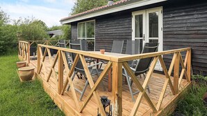 A wooden deck with outdoor furniture, a chimney, and a house with dark siding and a red-tiled roof. - 8 Person Holiday Home in Stege (Stege)