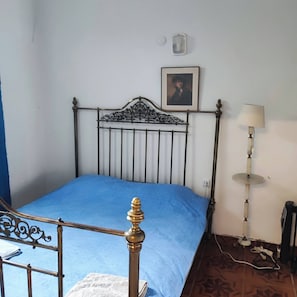 Une chambre à coucher avec un lit en métal, une couvre-lit bleue, un tableau encadré au mur, une lampe de chevet et un radiateur.