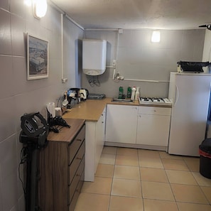 Une cuisine compacte équipée d’une cuisinière à gaz, d’un réfrigérateur, d’un évier et d’un plan de travail sur lequel sont disposés divers objets.