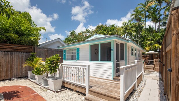 A small, single-story house with a porch, a fenced yard, and a pathway leading to the house. - Shared Pool + Backyard Lounge | Charming Cottage | Steps to Waterfront Dining (Key West)