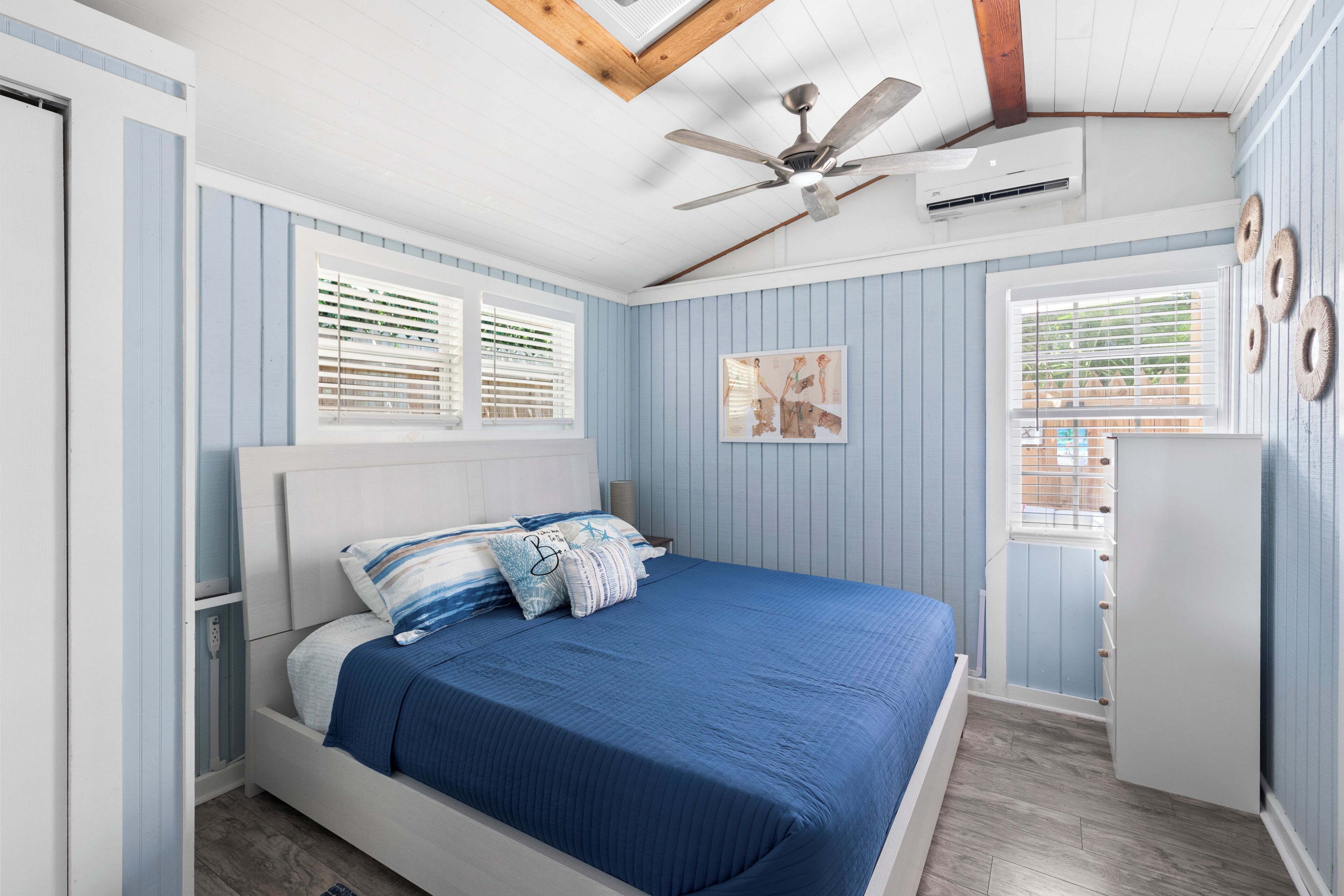 Une chambre à coucher comprenant un lit, un ventilateur de plafond, un appareil de climatisation et une fenêtre avec des stores.