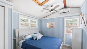 A bedroom with a bed, a ceiling fan, an air conditioning unit, and a window with blinds. - Shared Pool + Backyard Lounge | Charming Cottage | Steps to Waterfront Dining (Key West)