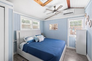 Ein Schlafzimmer mit einem Bett, Deckenventilator, Klimaanlage und einem Fenster mit Jalousien.