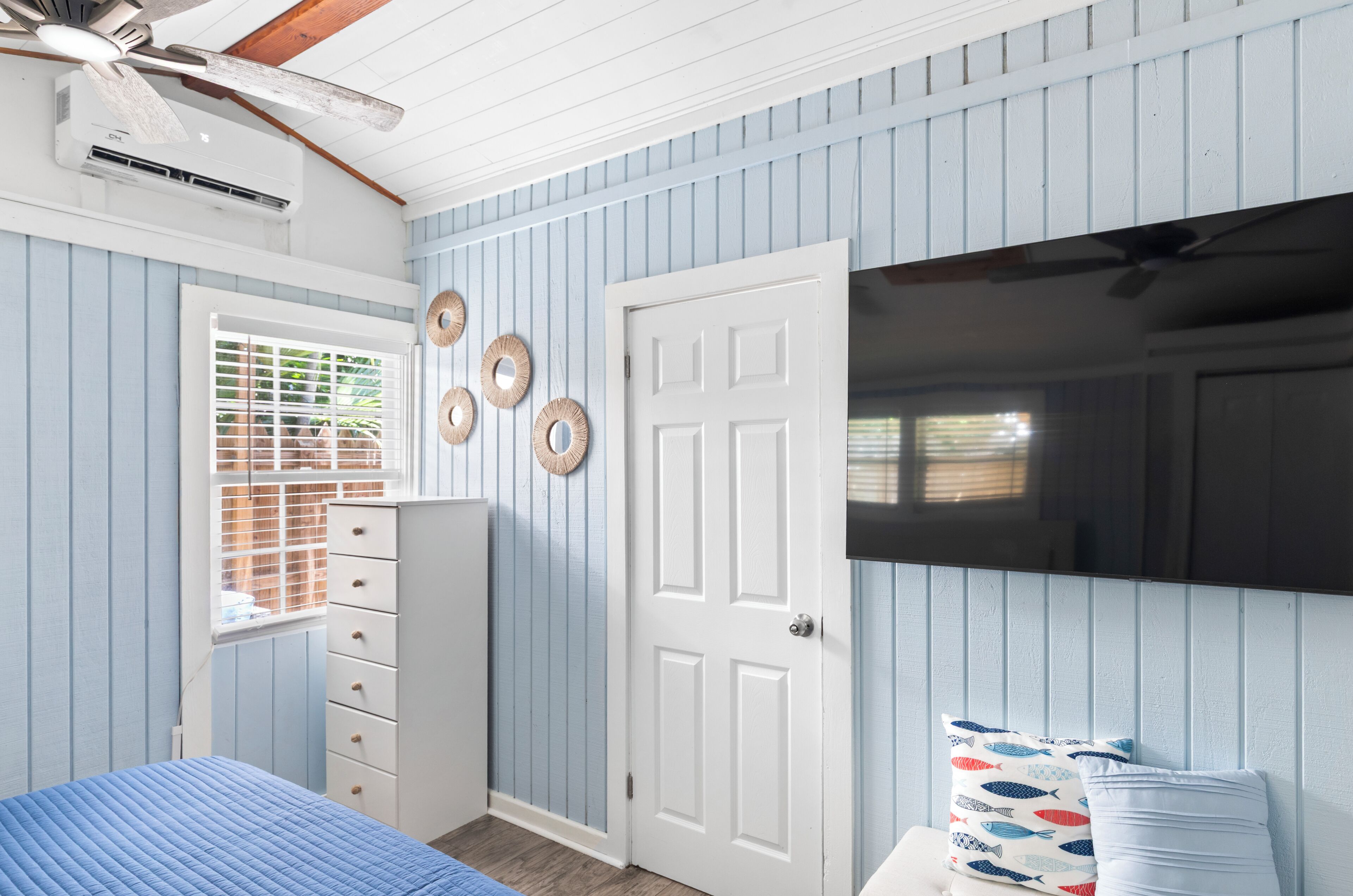 A bedroom with a bed, a dresser, a door, a window with blinds, and wall decorations.