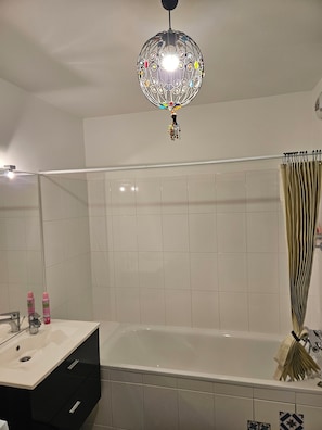 Ein Badezimmer mit weißem Waschbecken, einer Badewanne, einer Duschkabine aus Glas und einer dekorativen Pendelleuchte.